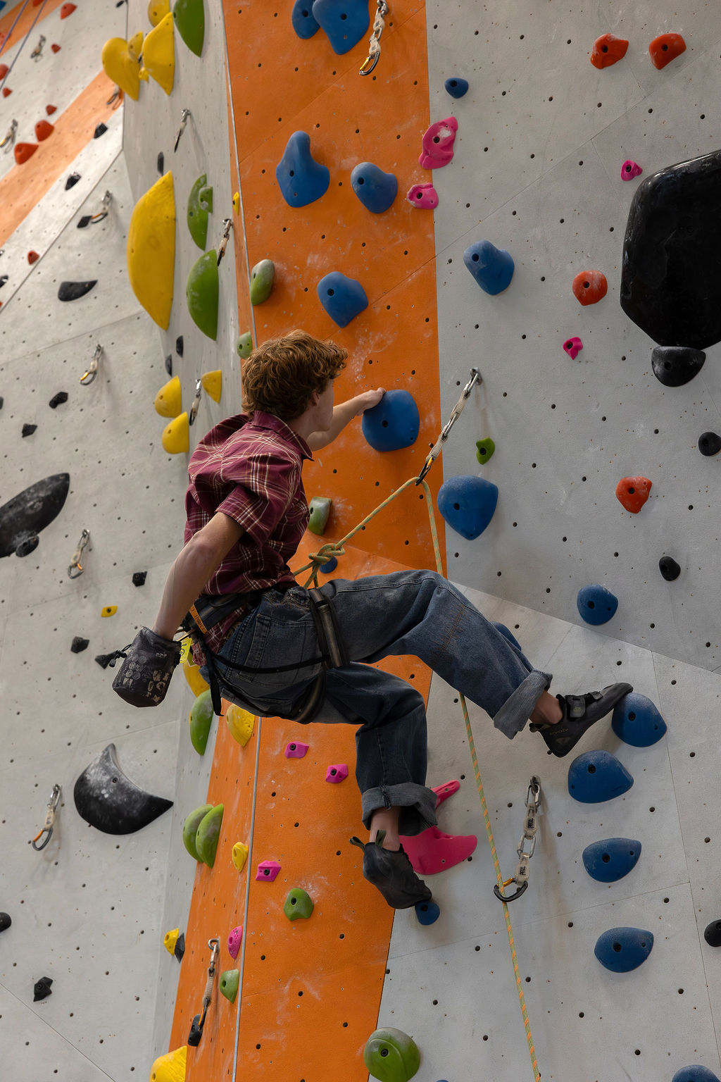 Cash mid-route on the climbing wall, reaching for a blue hold