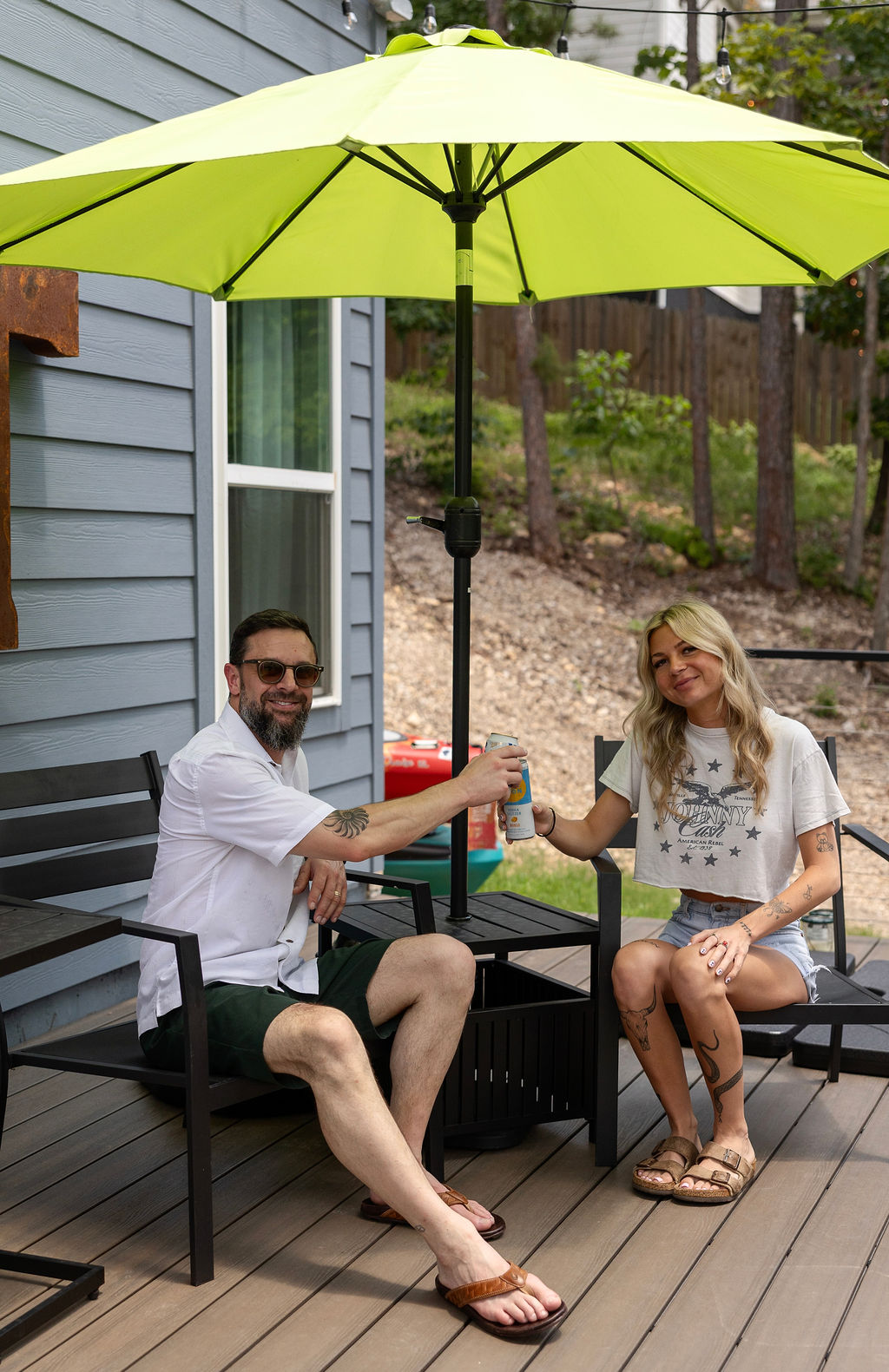 Jordan and Cody toasting cans under a bright green umbrella on a deck