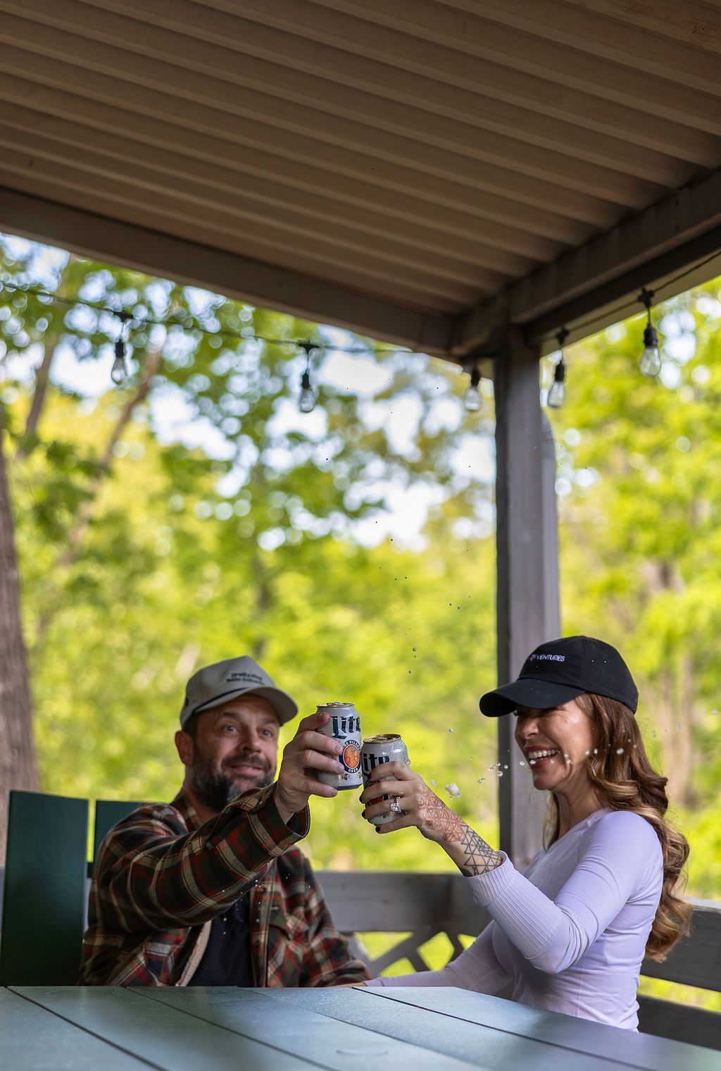 Ashley in a Refract Ventures cap laughing with Cody over a toast on the Little Sugar porch